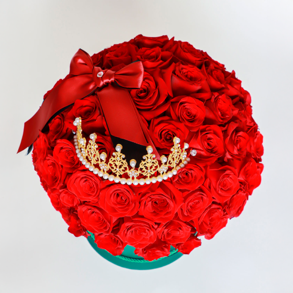 Arreglo floral de rosas rojas en caja verde con corona dorada decorativa.