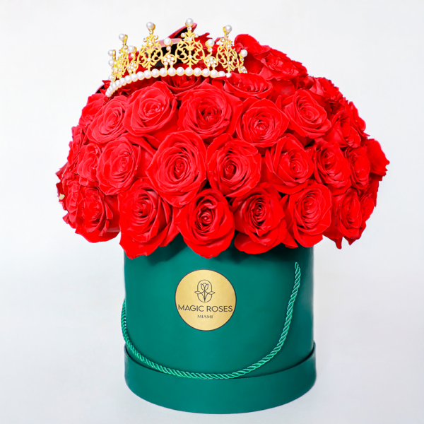 Arreglo floral de rosas rojas en caja verde con corona dorada decorativa.