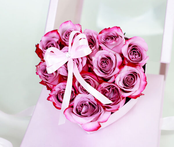 Arreglo floral en forma de corazón rosa con rosas frescas y lazo decorativo.