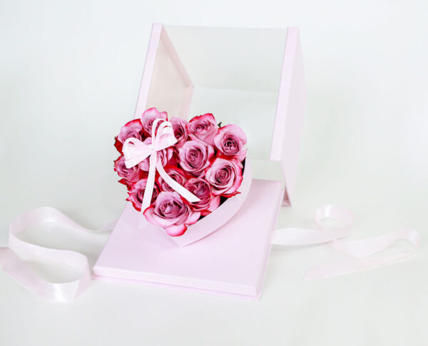 Arreglo floral en forma de corazón rosa con rosas frescas y lazo decorativo.