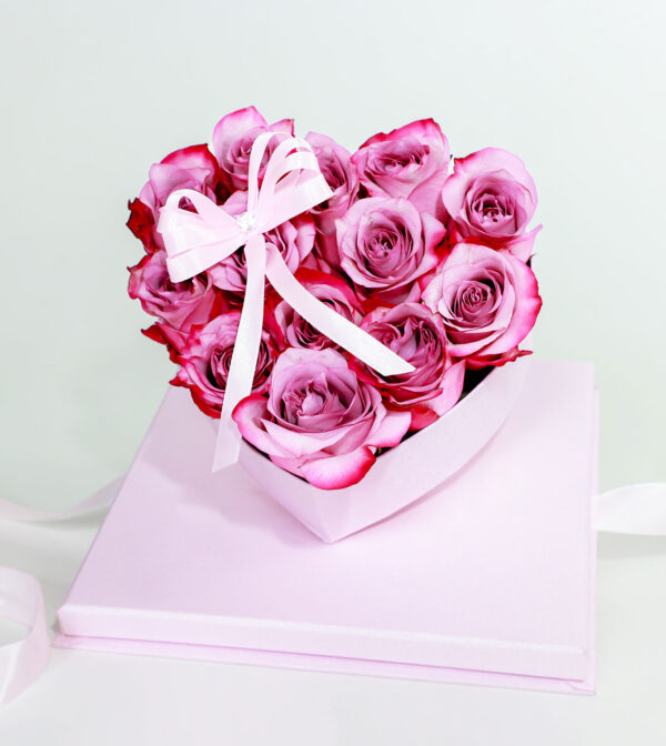 Arreglo floral en forma de corazón rosa con rosas frescas y lazo decorativo.