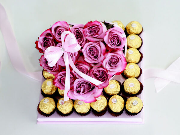 Arreglo floral en forma de corazón con rosas rosadas frescas y una caja de bombones Ferrero Rocher.