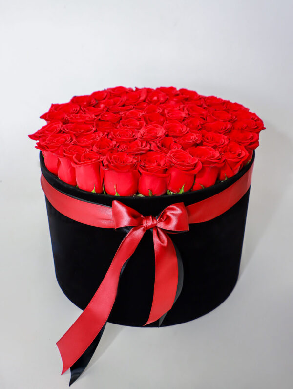 Arreglo floral de rosas rojas frescas en caja negra con lazo rojo decorativo.