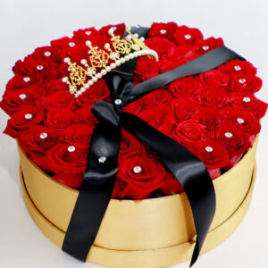 Caja dorada con rosas rojas frescas, decorada con brillantes y una corona dorada con perlas, complementada con un lazo negro