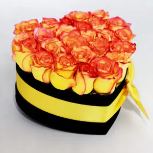 Caja en forma de corazón con rosas amarillas y naranjas, decorada con un lazo amarillo sobre fondo blanco